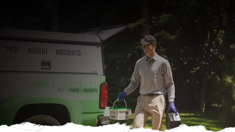 Pest control worker carrying equipment next to a branded truck in a sunny outdoor setting.