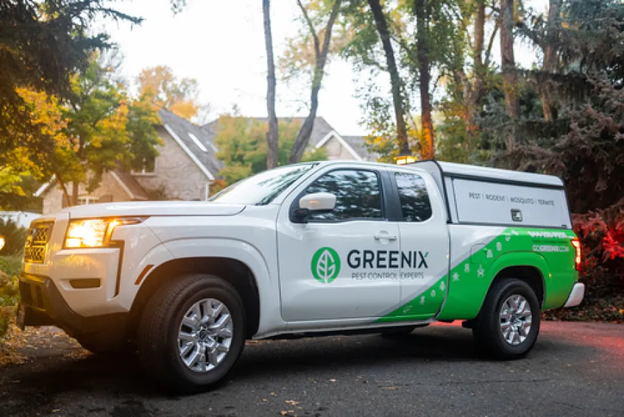 White pickup truck with Greenix pest control branding parked in a suburban neighborhood during autumn.
