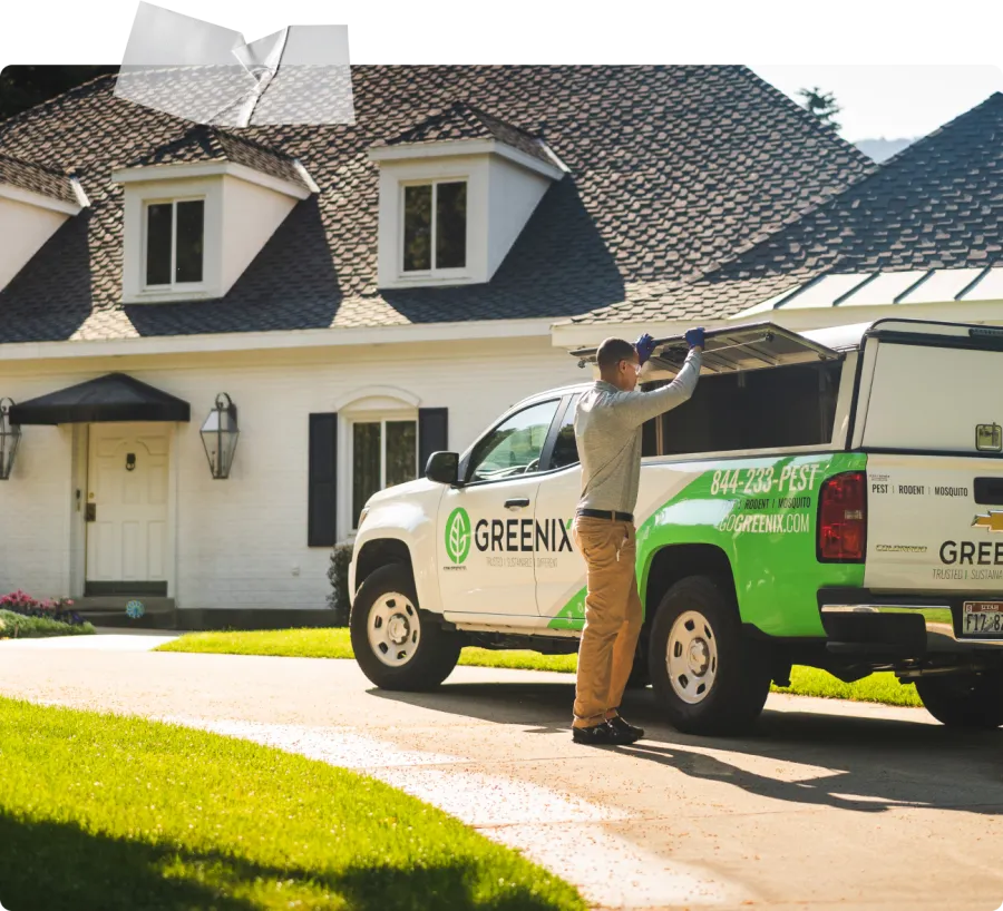 Technician preparing equipment from Greenix pest control truck outside suburban house on sunny day