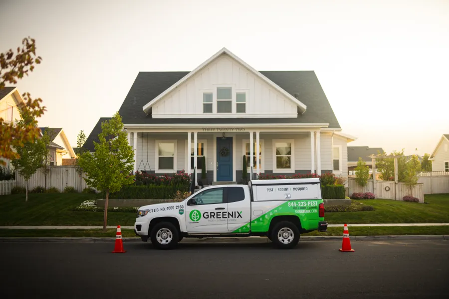 Greenix pest control truck parked in front of a white suburban house with a blue door during daytime.
