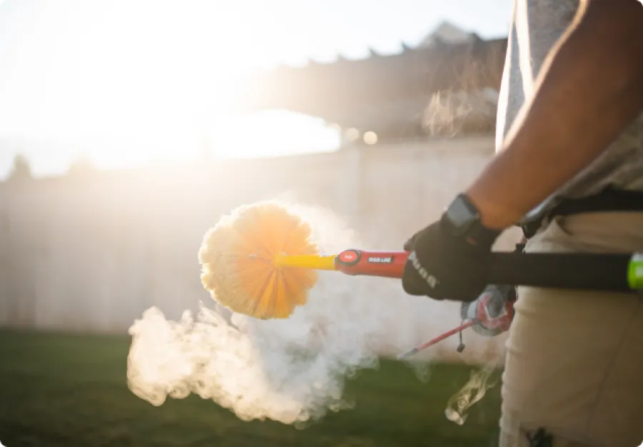 Person using a gas-powered cleaning brush emitting steam in a backyard during daylight.