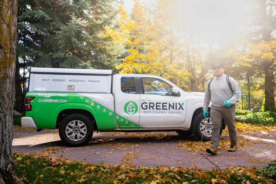 Greenix pest control truck parked outdoors with technician walking beside it in autumn setting