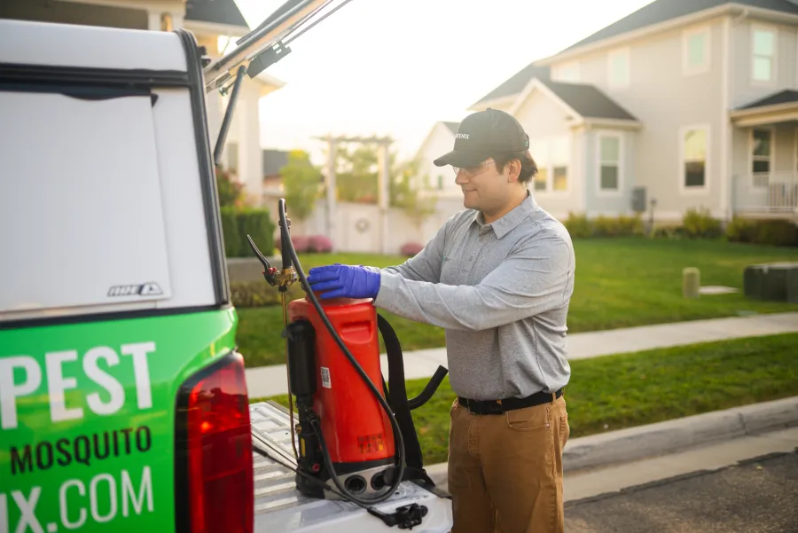 Pest control worker wearing gloves handling spray equipment on a truck in a suburban neighborhood.
