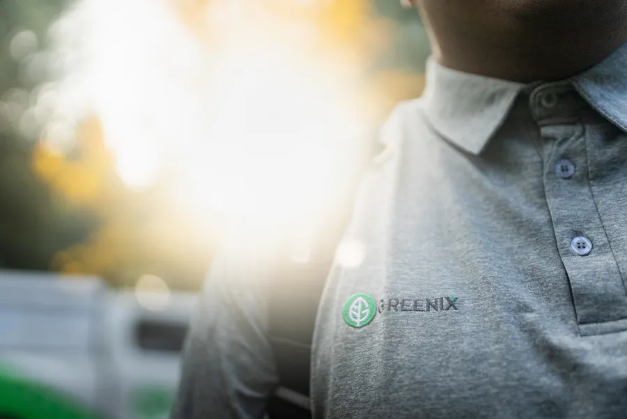 Close-up of a person wearing a Gray Greenix polo shirt with sunlight in the background