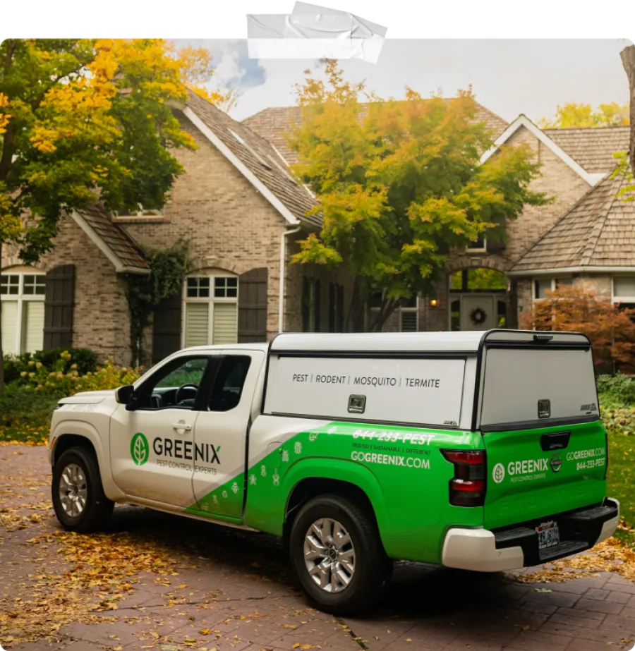 Greenix pest control truck parked in front of a suburban brick house with autumn trees.