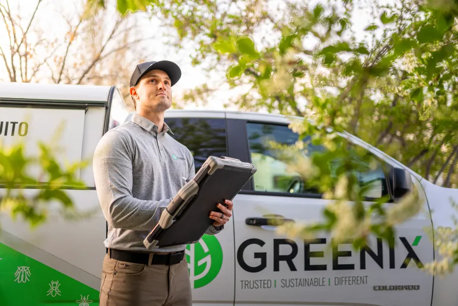 Greenix technician assessing outdoor treatment with vehicle in background, showcasing pest control services.