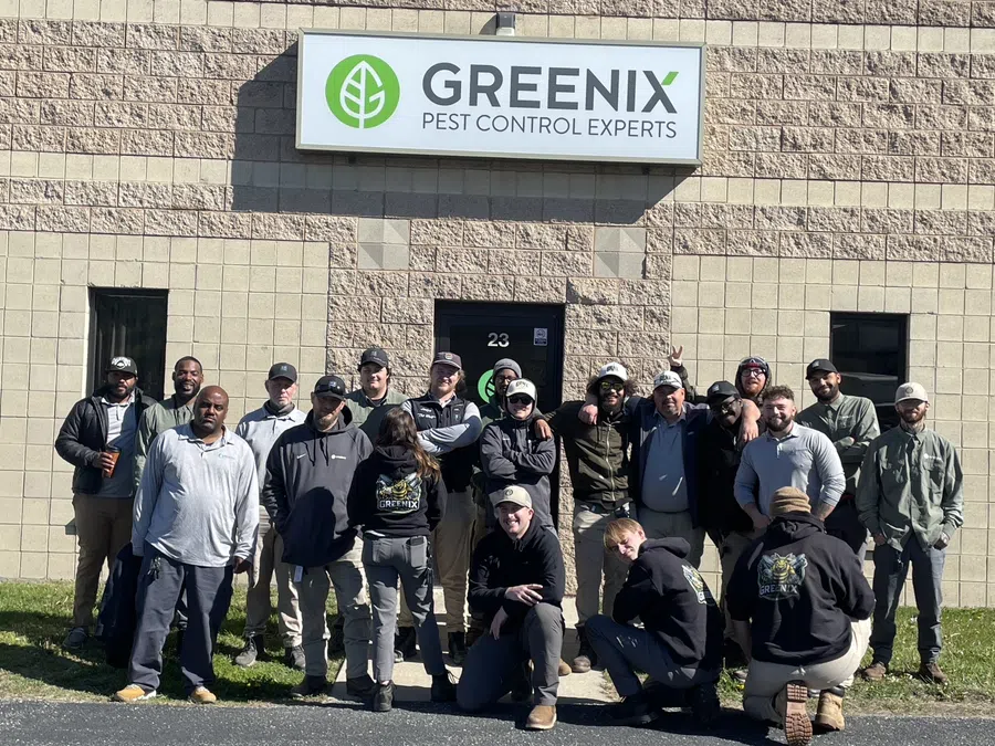 Group photo of Greenix Pest Control experts standing outside the company building under the Greenix sign