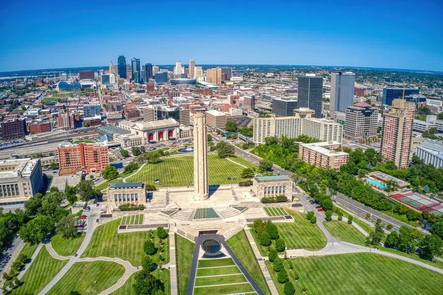 Aerial view of Kansas City skyline with Liberty Memorial and lush city park under clear blue sky.