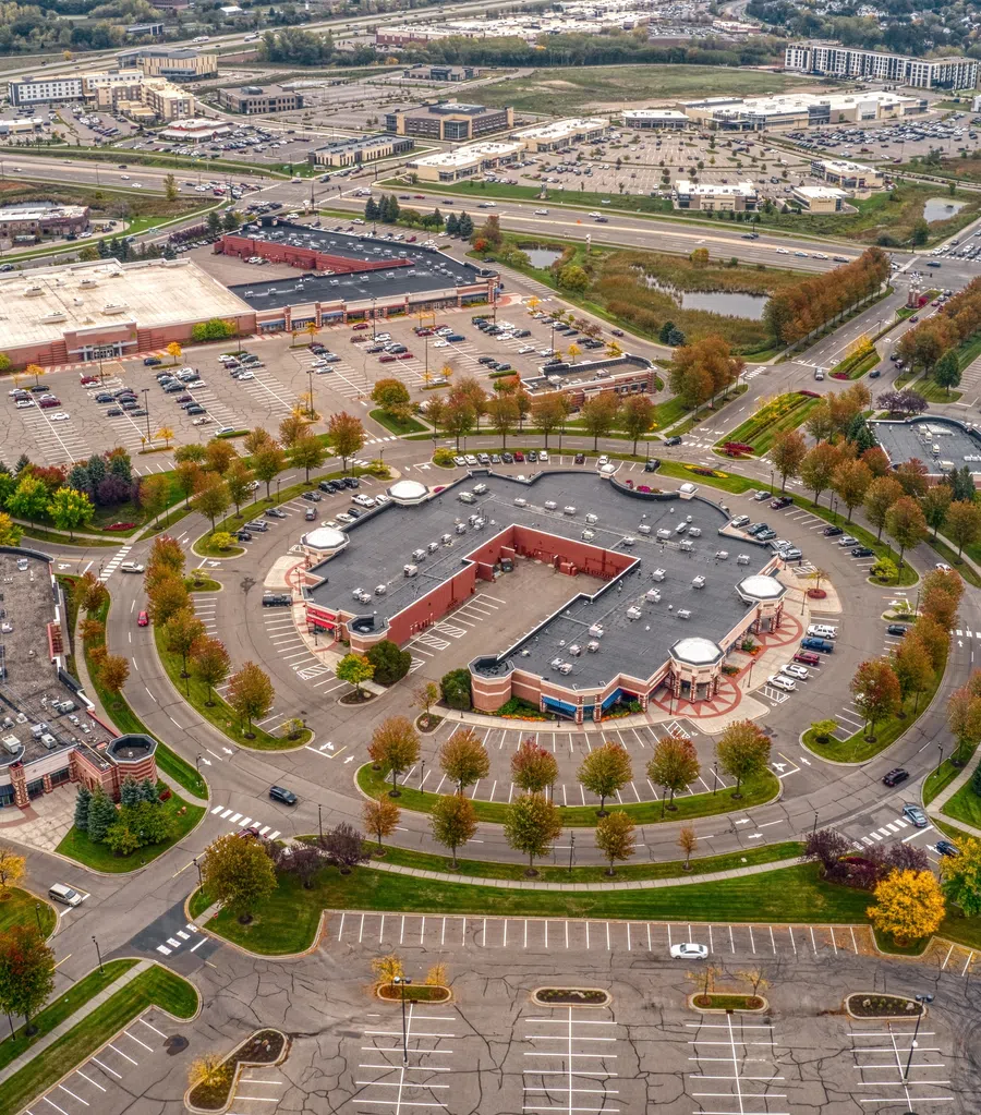 Aerial view of a circular shopping plaza with parking lots, roads, and surrounding commercial areas in autumn.