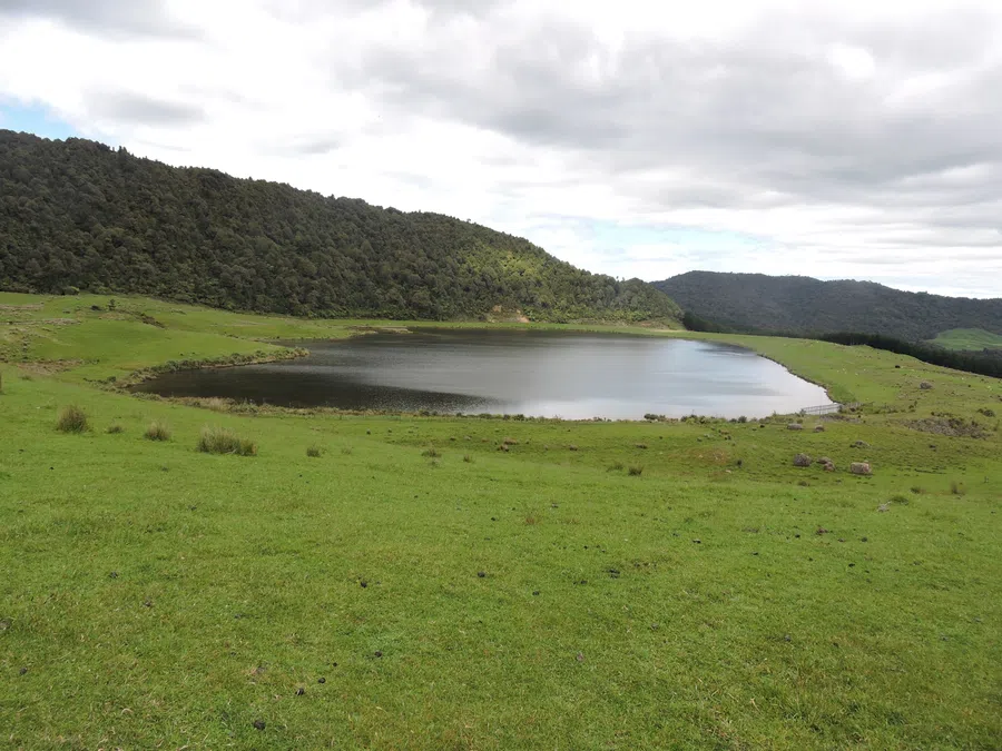 Tranquil lake surrounded by lush green hills and cloudy sky in a serene natural landscape.