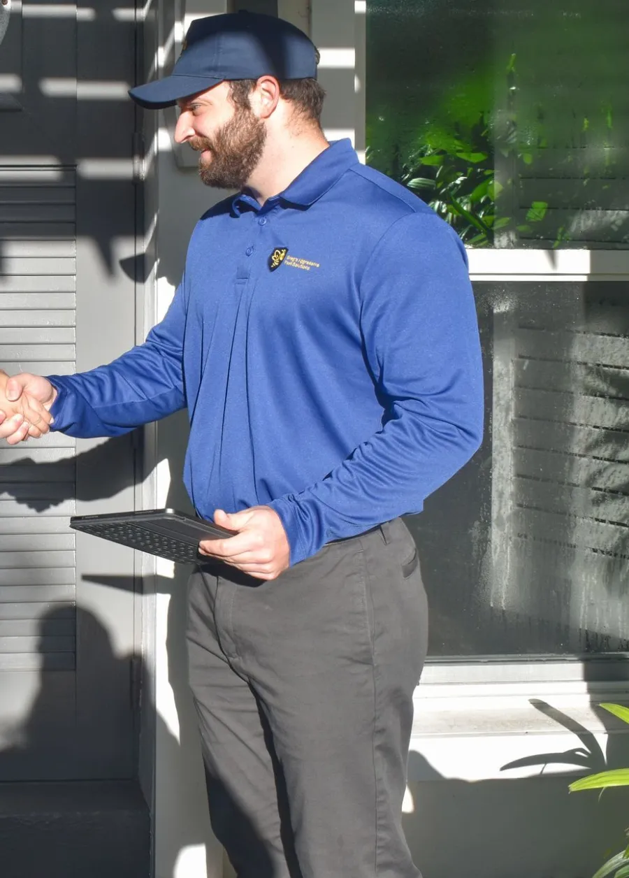 Man in blue uniform and cap shaking hands while holding a tablet outside in bright daylight.