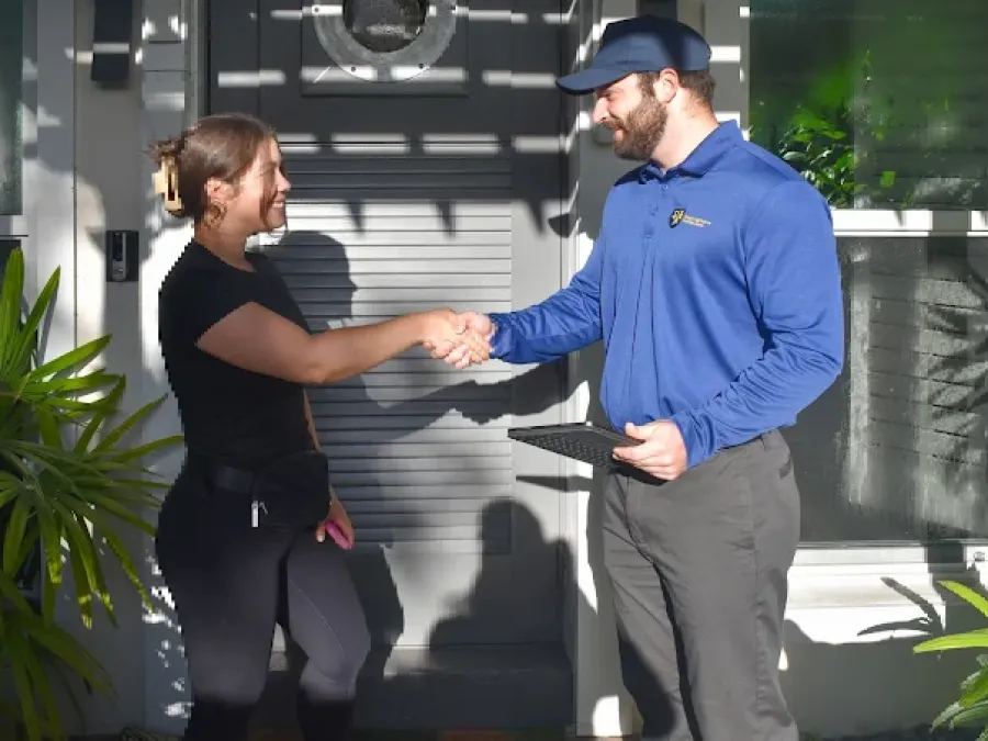 Man in blue shirt shaking hands with woman outside home door during daytime with plants around