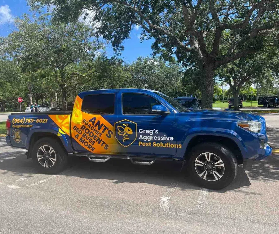 Blue truck with Greg's Aggressive Pest Solutions logo and contact info parked under trees on a sunny day.