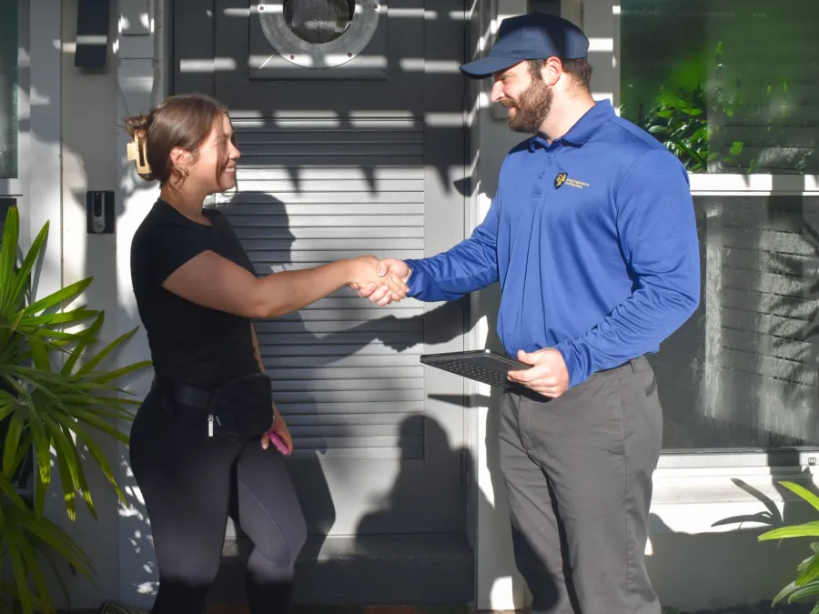 Woman and technician shaking hands outside a house during a home service visit on a sunny day.