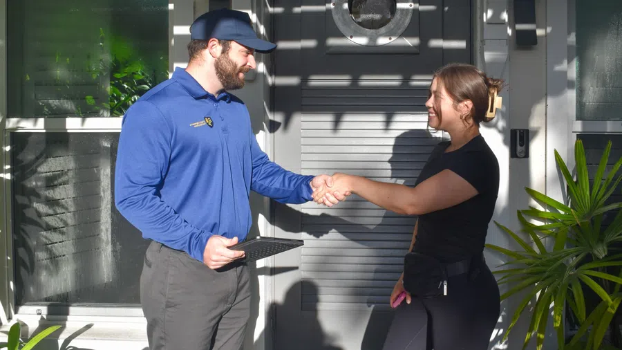 Delivery man in blue uniform shaking hands with woman outside her home with a tablet in hand.