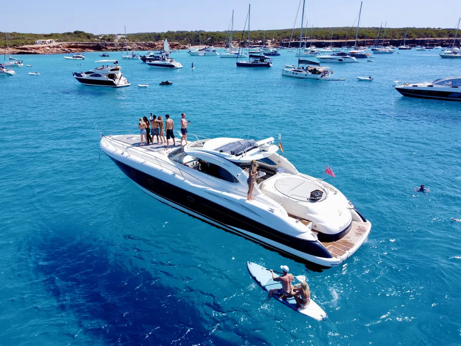 Group of people enjoying a luxury yacht on clear blue water with several boats anchored nearby.