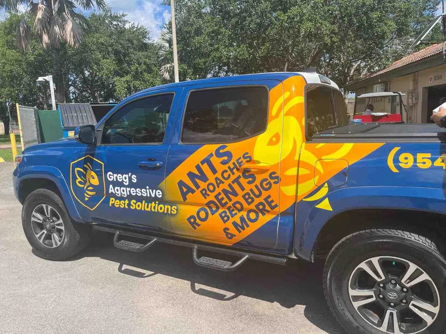 Blue and yellow pest control truck for Greg's Aggressive Pest Solutions listing ants, roaches, rodents, bed bugs, and more.