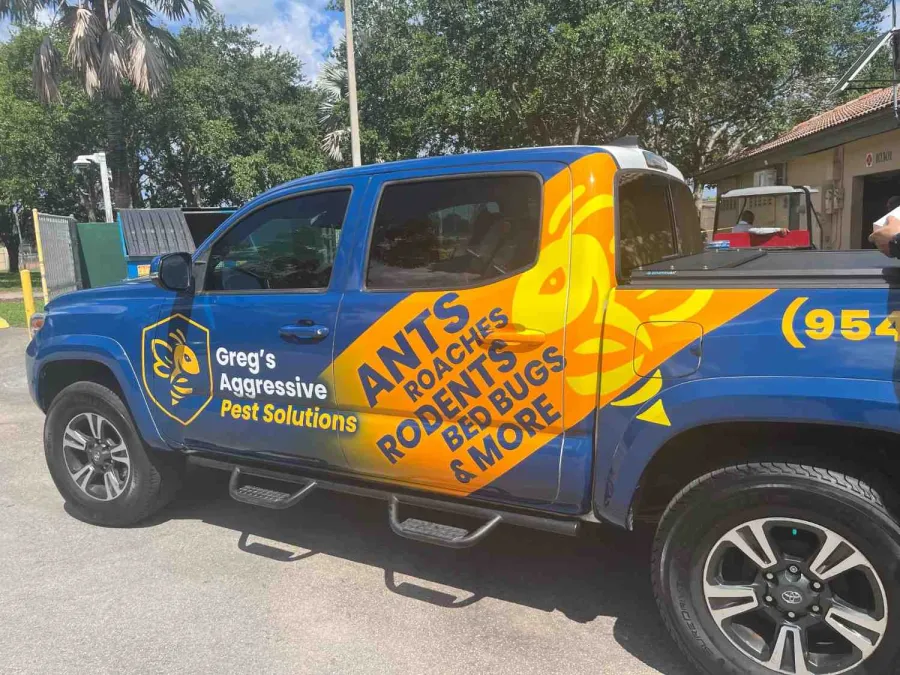 Blue and yellow pest control truck with Greg's Aggressive Pest Solutions branding and insect illustrations.