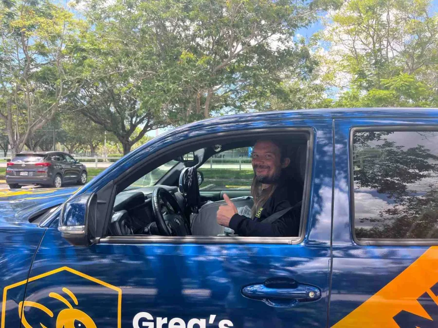 Smiling man gives thumbs up sitting in the driver's seat of a blue vehicle with company logo on the door.