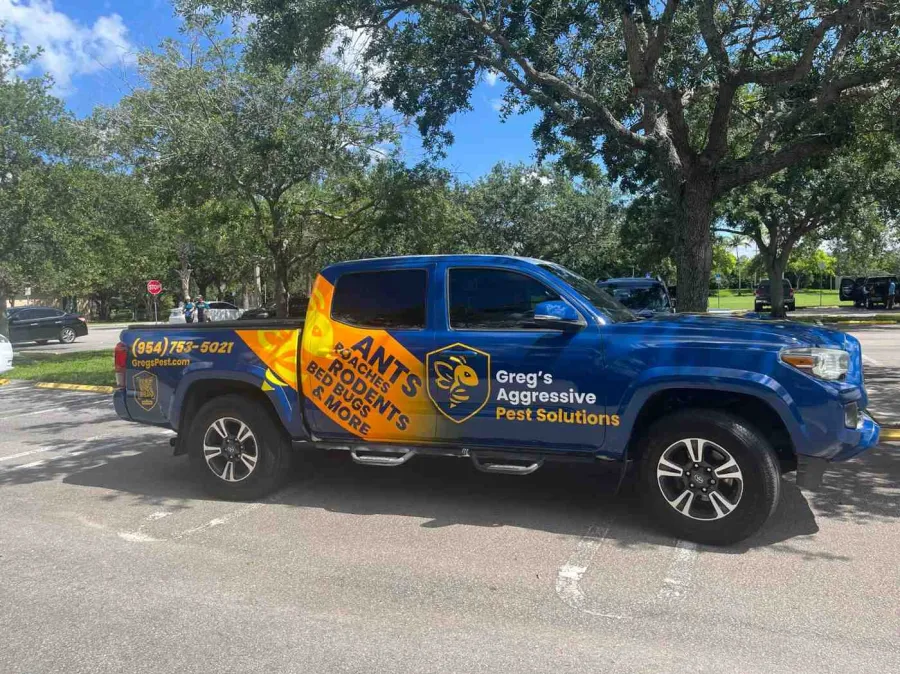 Blue truck with Greg's Aggressive Pest Solutions logo and contact info parked under trees on a sunny day.