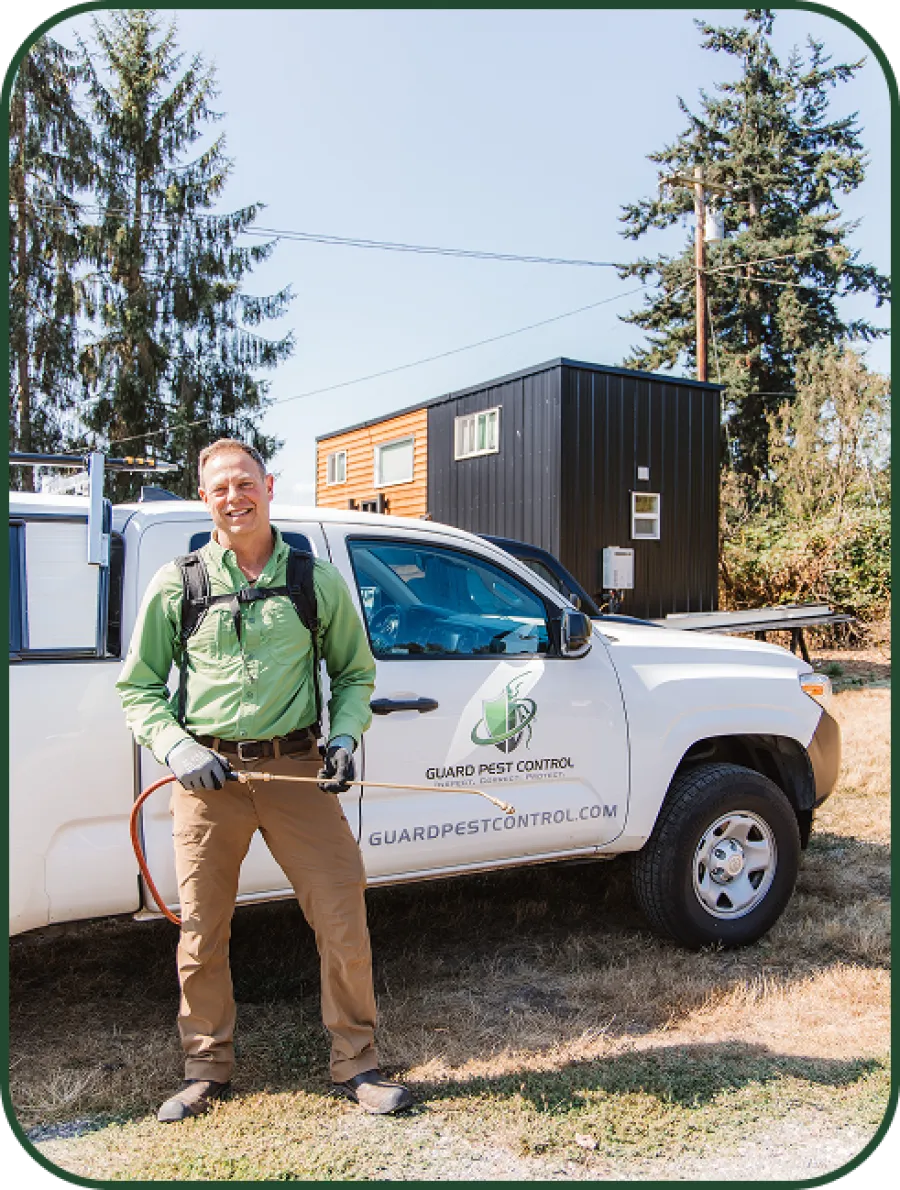Pest control technician in green shirt and gloves standing by Guard Pest Control truck with equipment.