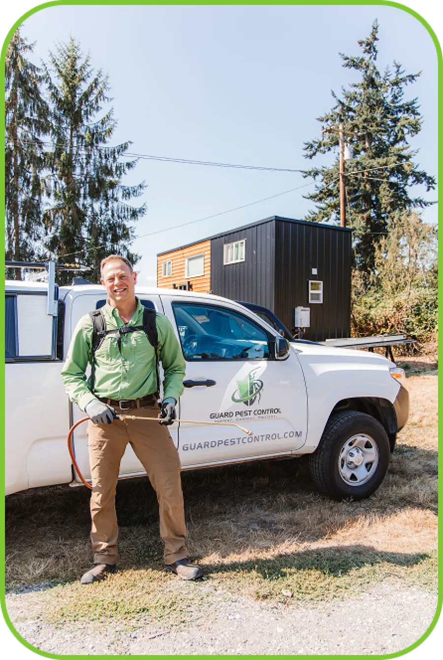 Pest control technician in green shirt standing by white Guard Pest Control truck outdoors during daytime.