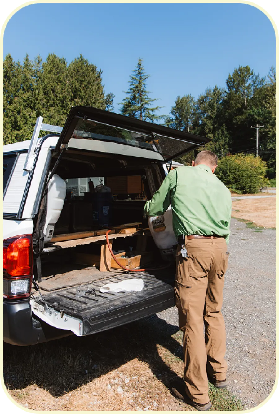 Man in green shirt loading tools into the back of a white pickup truck in a sunny outdoor setting.