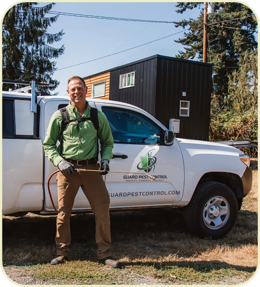 Pest control technician in green shirt and gloves standing by a white company truck outdoors on a sunny day.