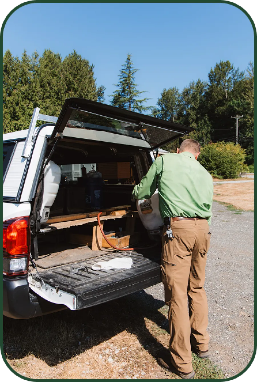 Man wearing green shirt and tan pants organizing tools in the back of a white utility truck outdoors on a sunny day