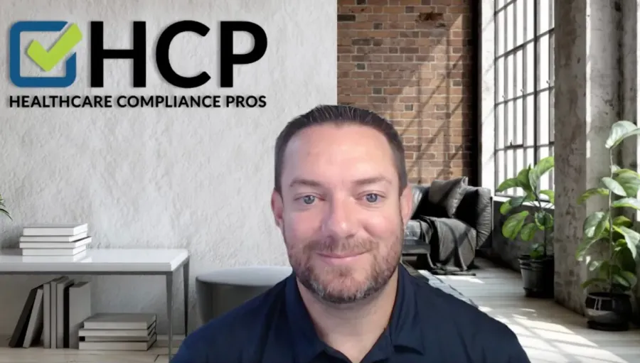 Man smiling in a modern office with Healthcare Compliance Pros logo on the wall and large windows letting in light.