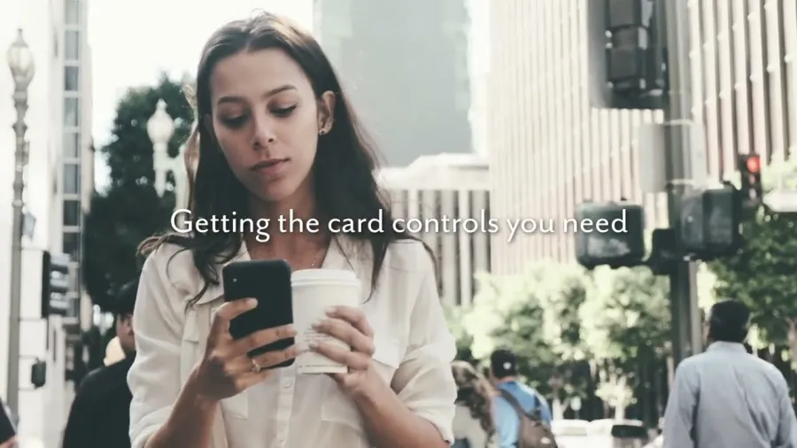 Young woman holding coffee and using smartphone outdoors in urban setting with card control text overlay