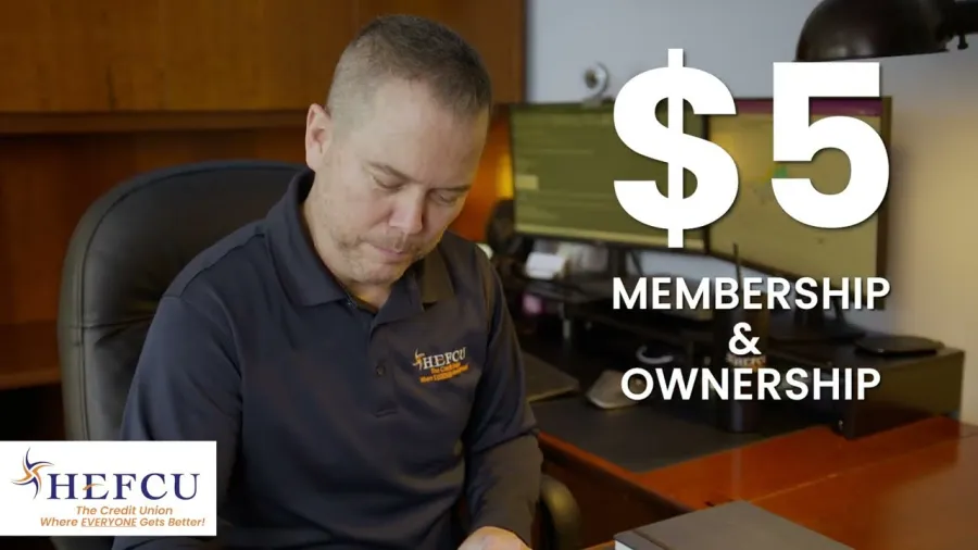 Man in office wearing HEPCU shirt with $5 membership and ownership text displayed on screen.