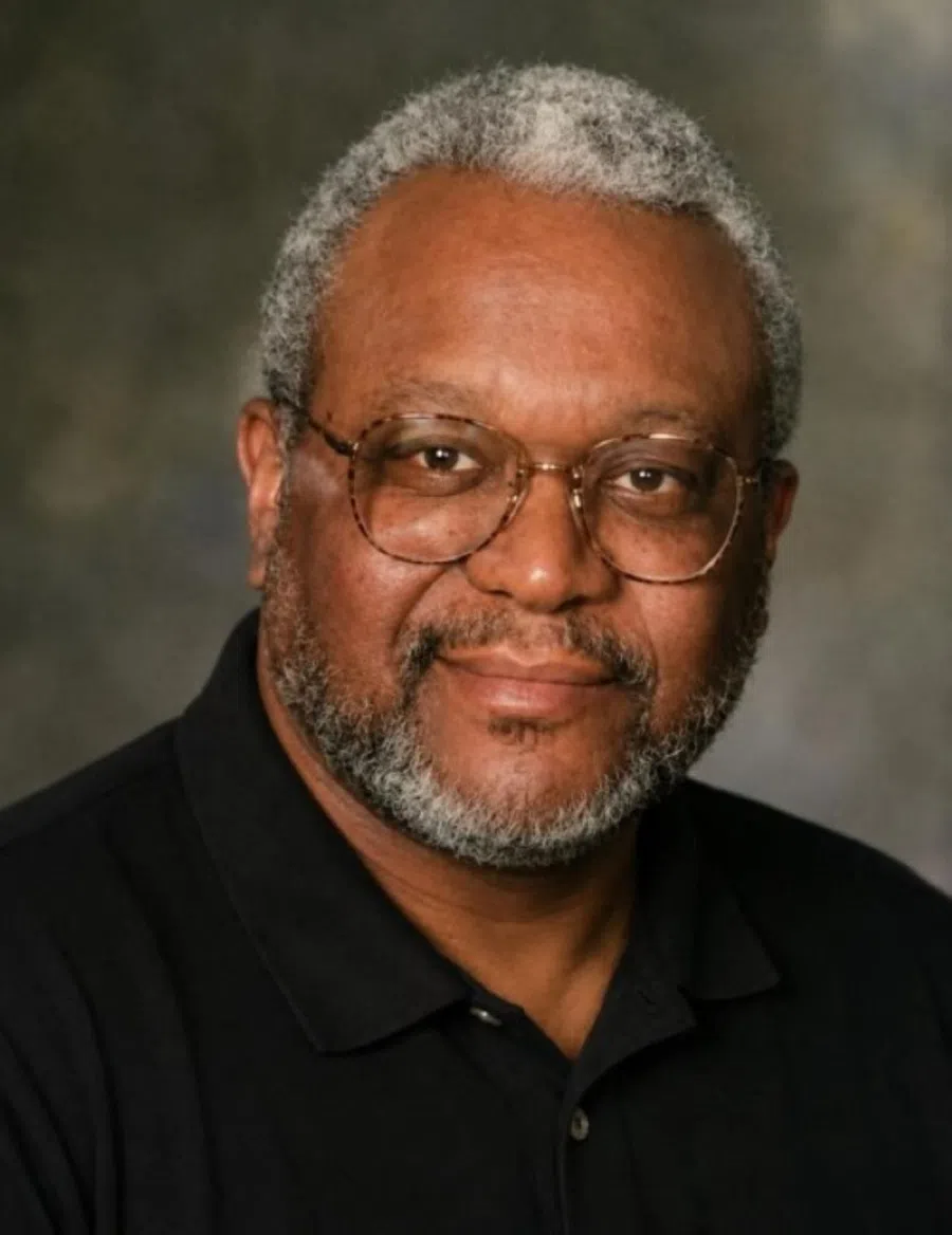 Portrait of a middle-aged man with gray hair and beard wearing glasses and a black shirt against a blurred background