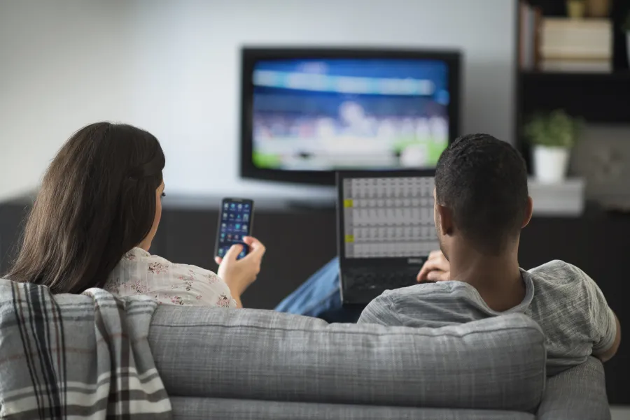 a woman holding a tv remote and man on laptop