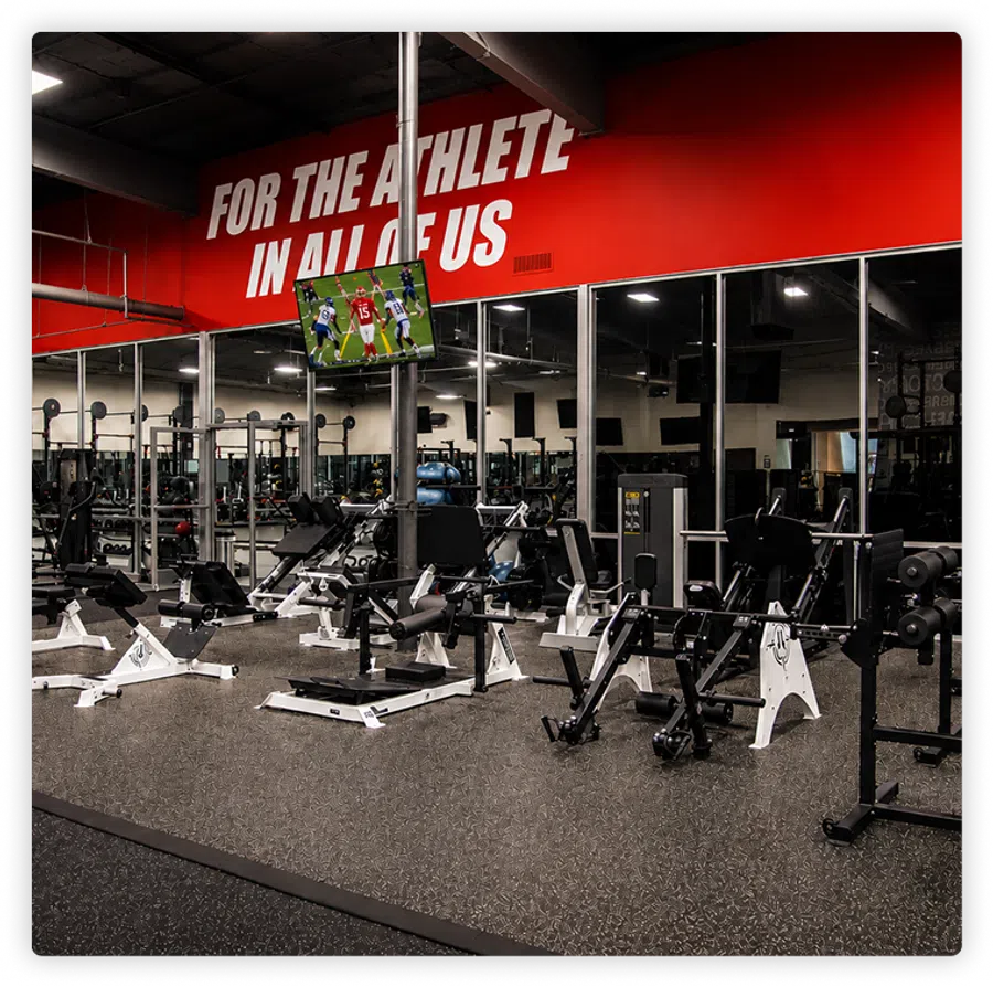 Modern gym interior with weight machines, mirrors, and motivational red wall stating For the athlete in all of us.