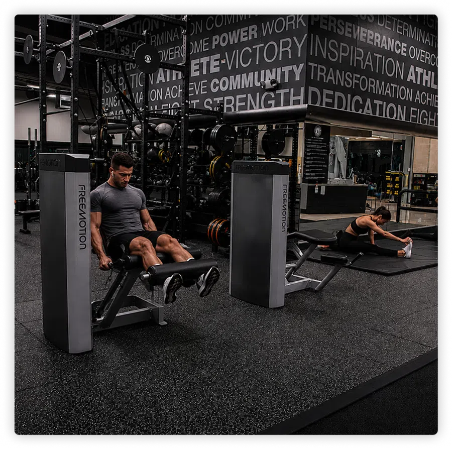 Man exercising leg extension machine and woman stretching on mat in modern gym with motivational wall text.
