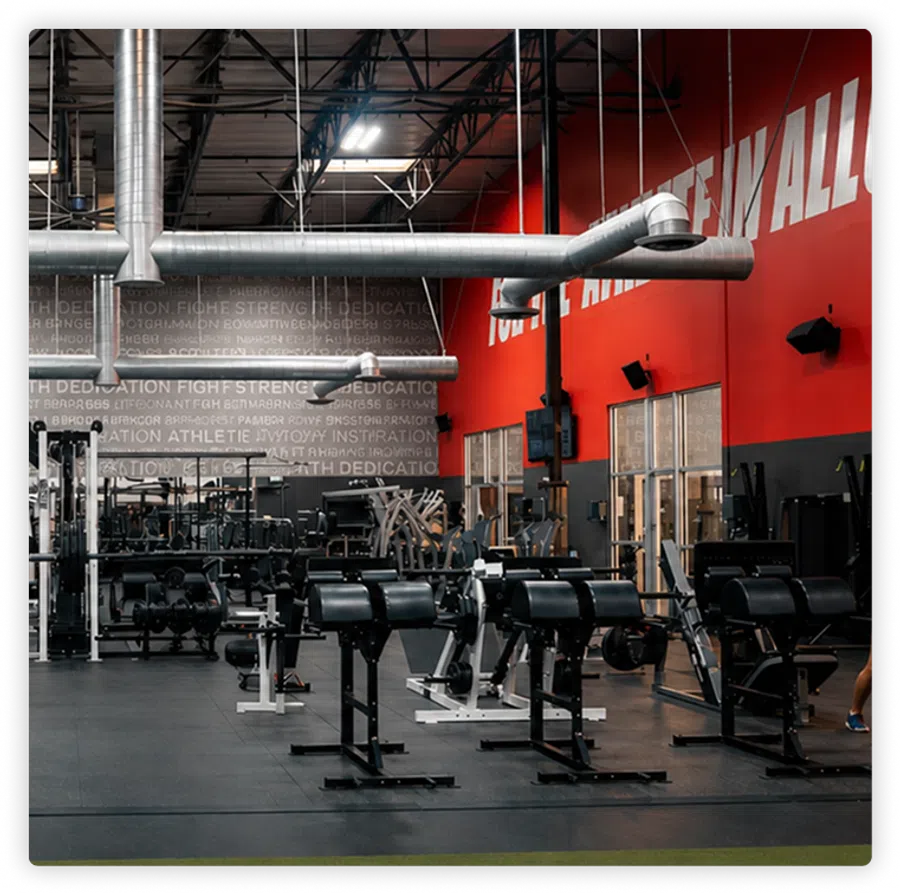 Spacious gym with weightlifting machines, black and red walls, and visible ventilation ducts overhead.