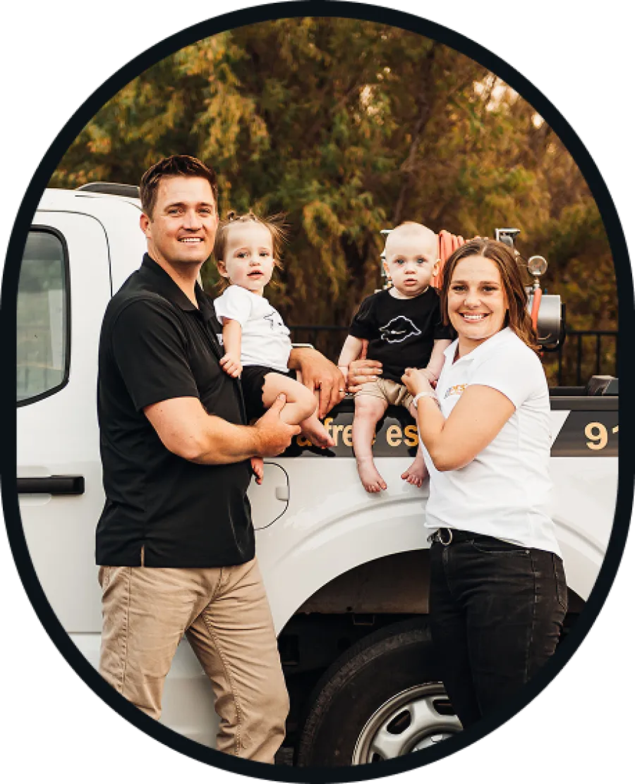 Family of four smiling and posing while holding two toddlers next to a white utility truck outdoors.