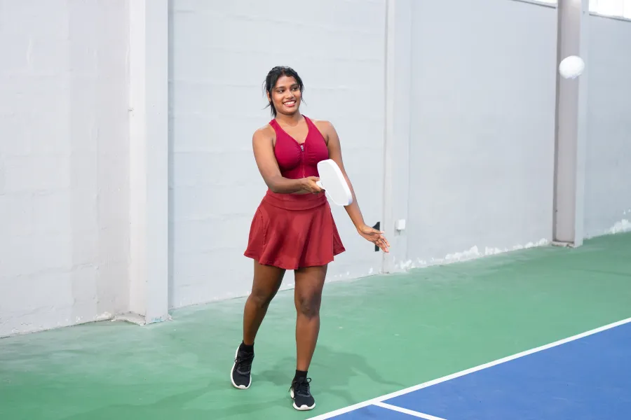 Close-up of player holding pickleball paddle and ball on blue outdoor court next to the net.