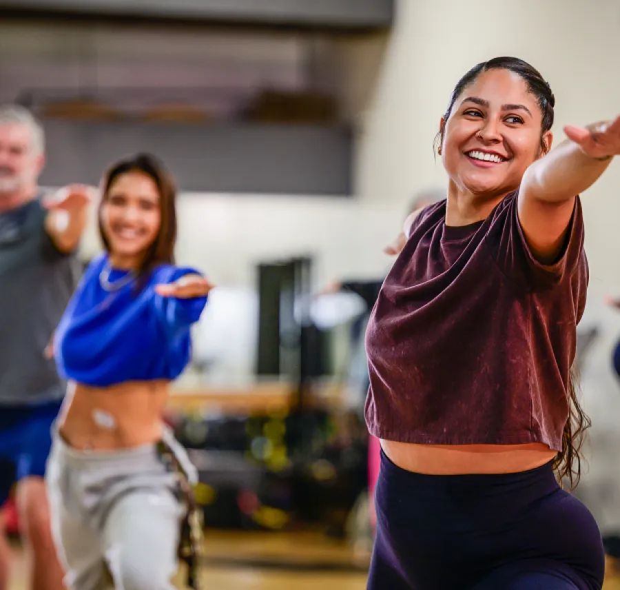 Group of diverse adults smiling and stretching arms forward in a vibrant indoor fitness class.