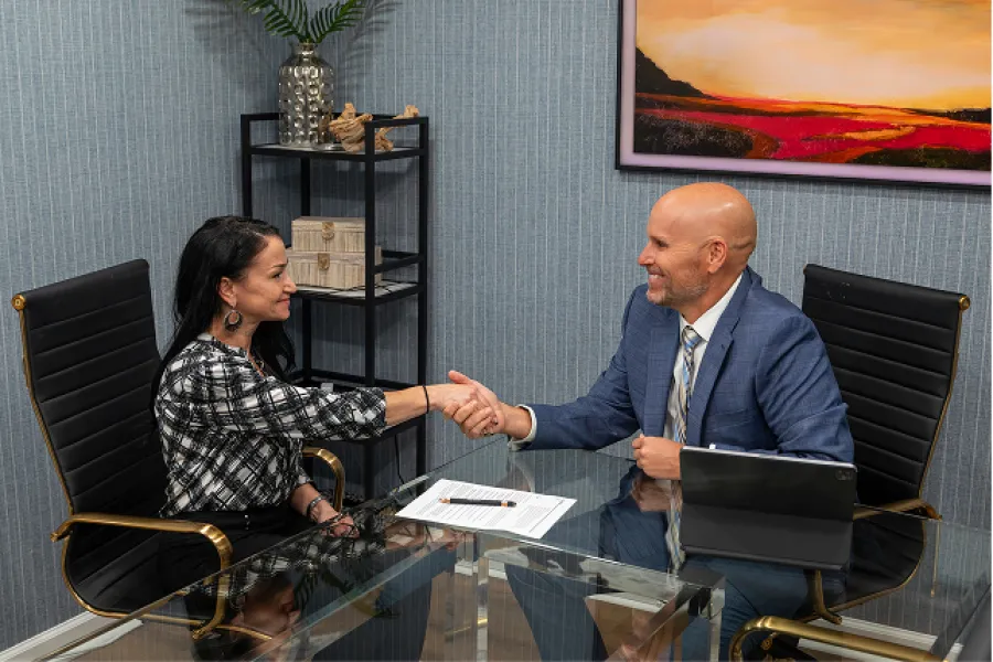 Businessman and businesswoman shaking hands during a meeting at a modern office with a glass table and artwork.
