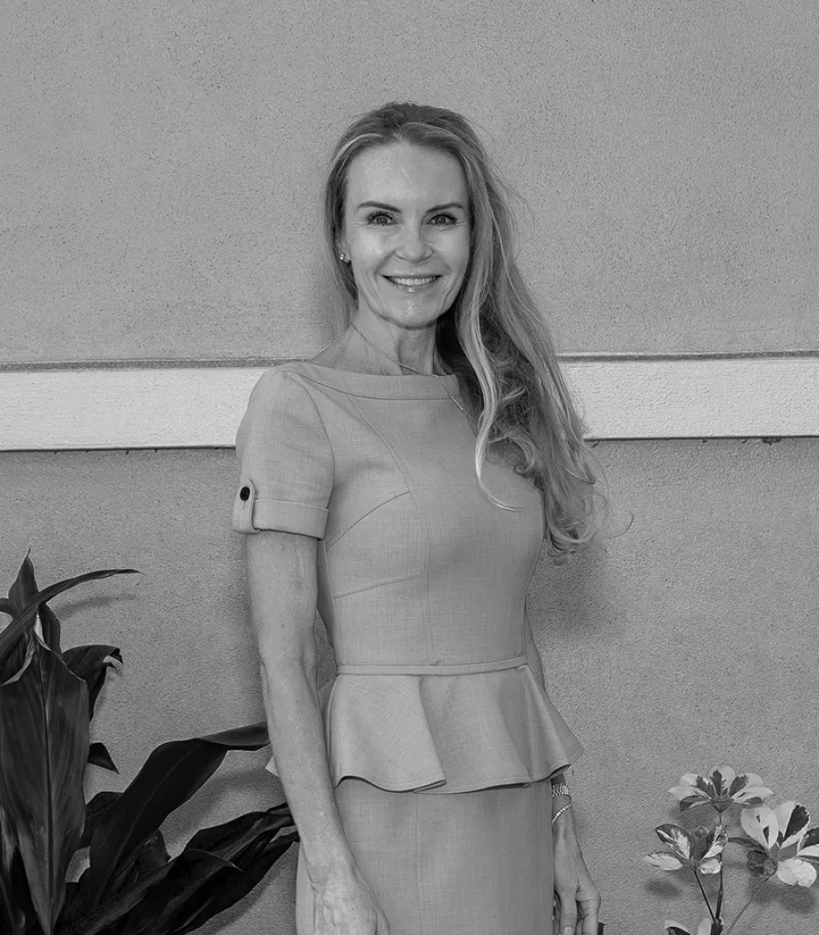 Smiling woman in a fitted dress with peplum detail standing by a textured wall and indoor plants