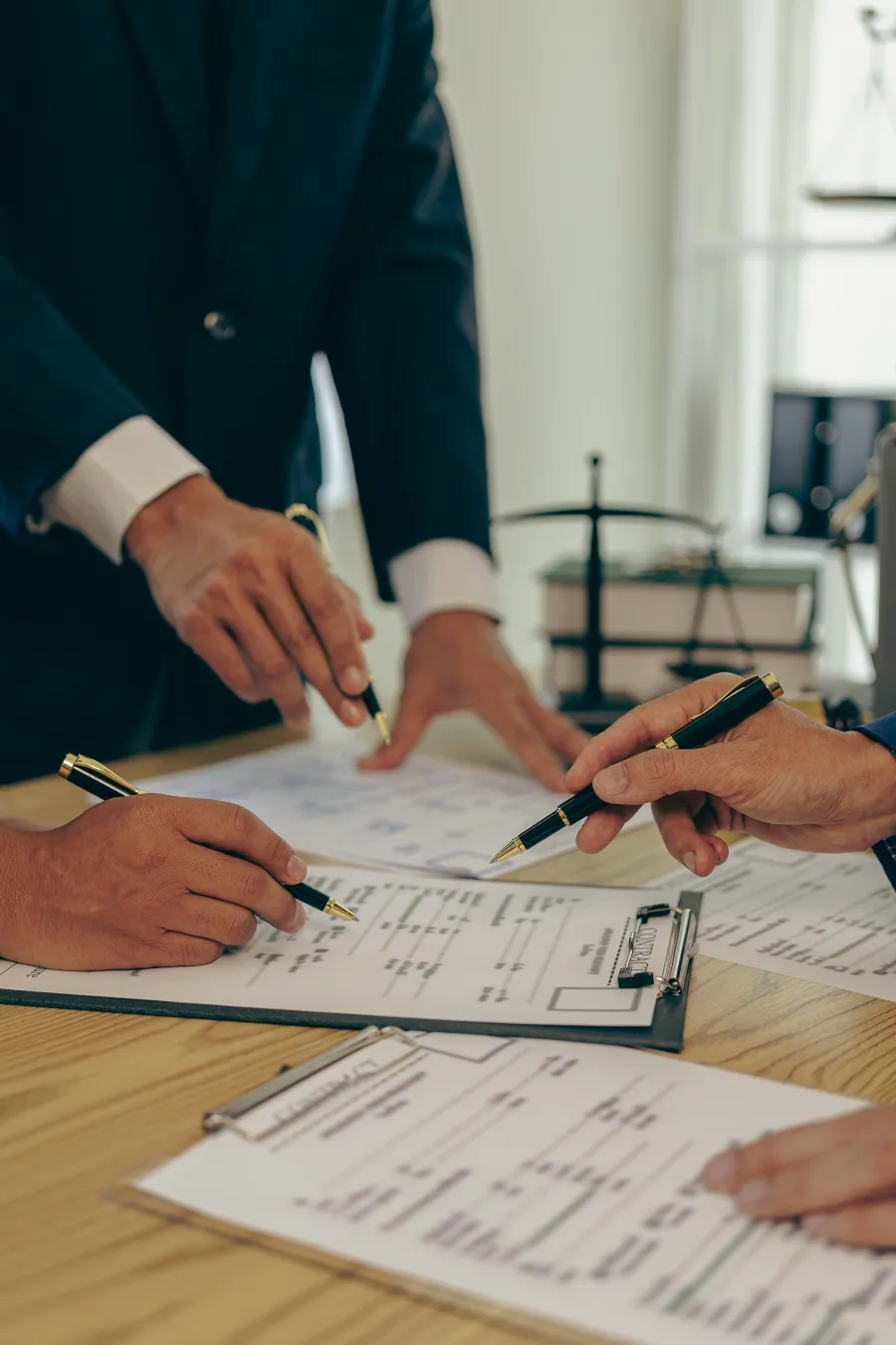 Business professionals reviewing and signing contracts on a wooden table with legal documents and pens.