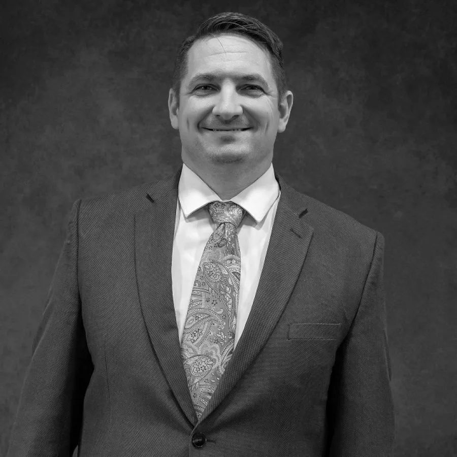 Black and white portrait of a smiling man in a suit and patterned tie against a textured backdrop.