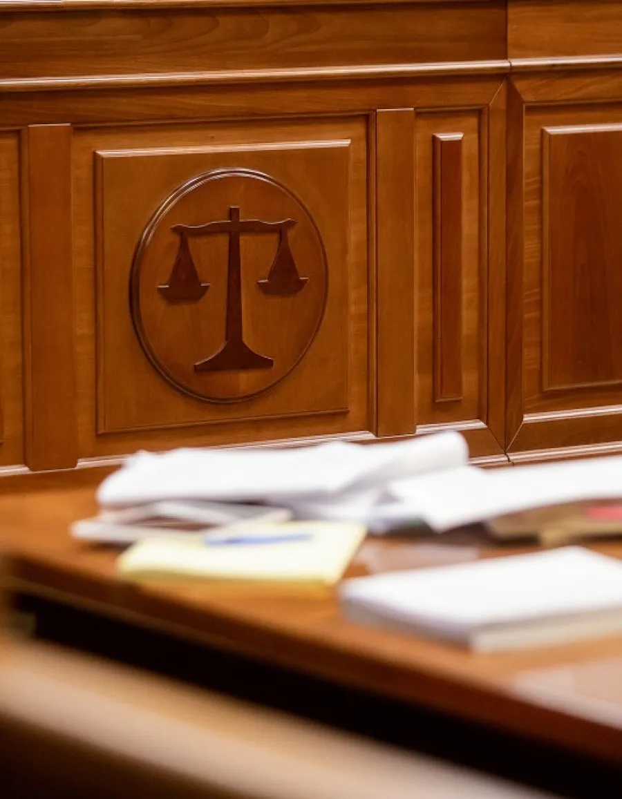 Close-up of a courtroom desk with legal documents, a microphone, and a wooden panel featuring justice scales.