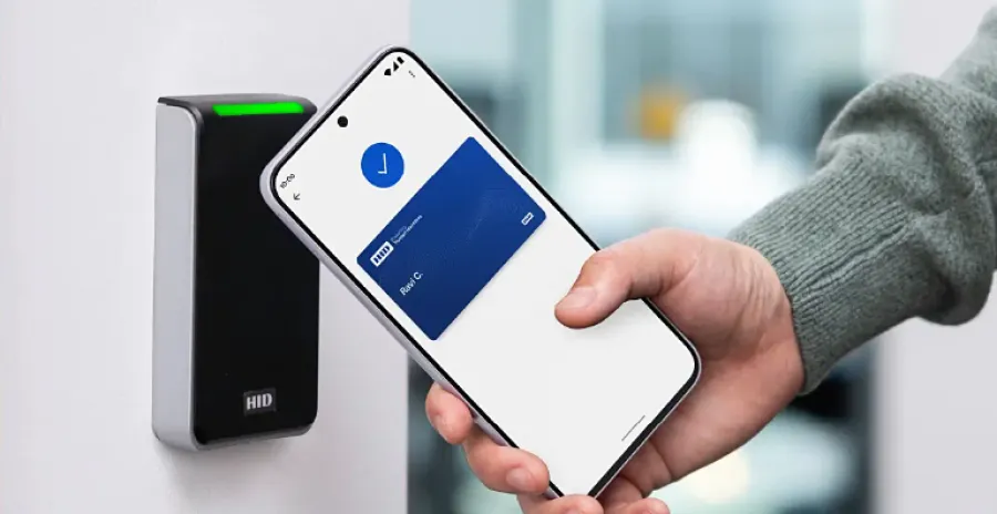 Hand holding smartphone with digital access card near HID reader for secure entry authorization.