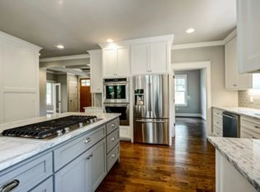 Modern kitchen with gray island, white cabinets, stainless steel appliances, and hardwood flooring in open layout