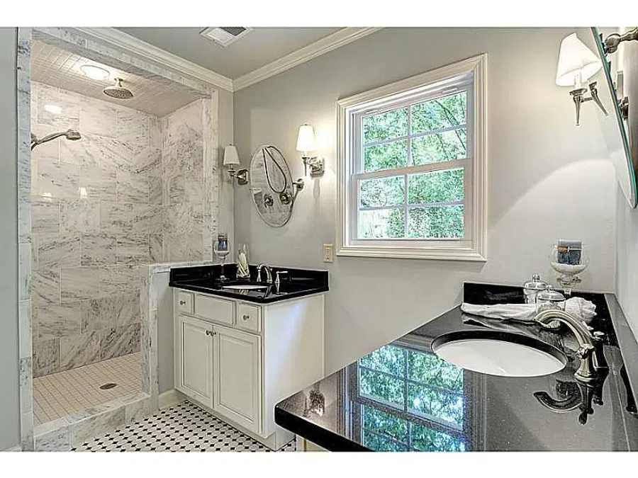 Modern bathroom with marble shower, dual sinks with black countertops, white cabinetry, and natural light from window.
