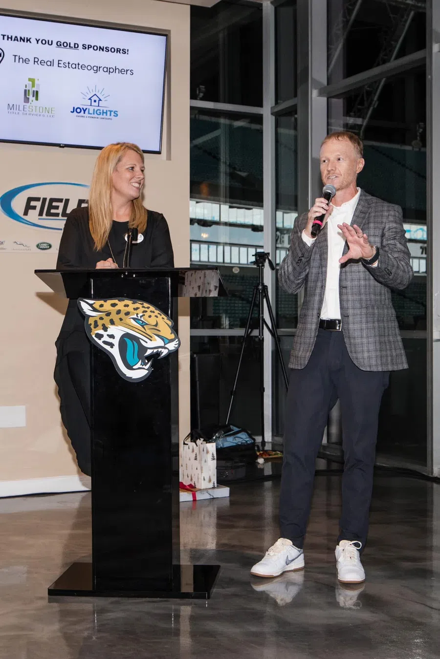 Brian and Kristin Lunsford speaking at a podium with a Jaguars logo in an indoor event at the stadium.
