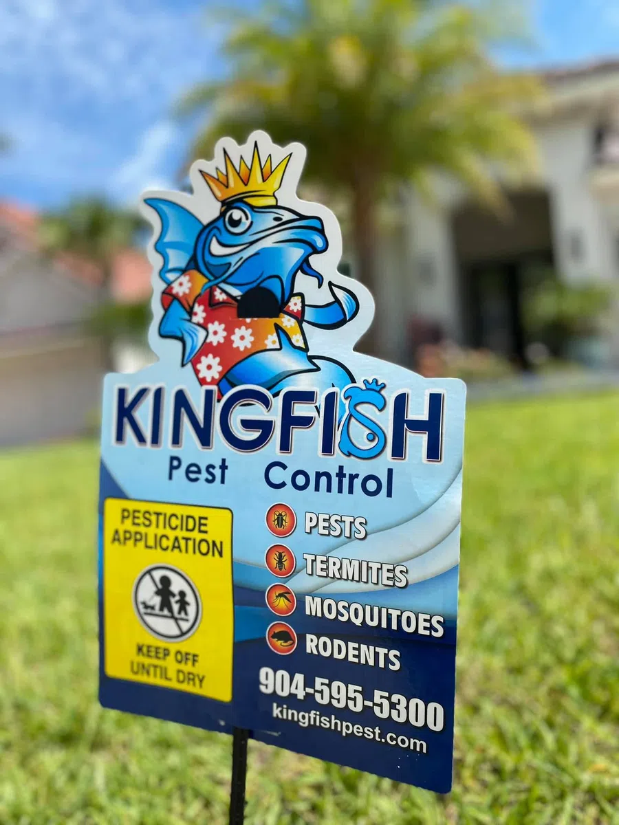 Kingfish Pest Control sign in yard with a cartoon fish wearing a crown and hawaiian shirt listing pests and contact details.